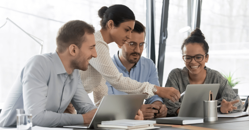 Training team in a boardroom with one member pointing at a laptop that they are all looking at.