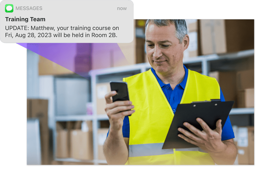 Man in yellow safety jacket with clip board and phone checks a message, a graphic overlay showing an automated training team update SMS from Administrate appears to left of image.